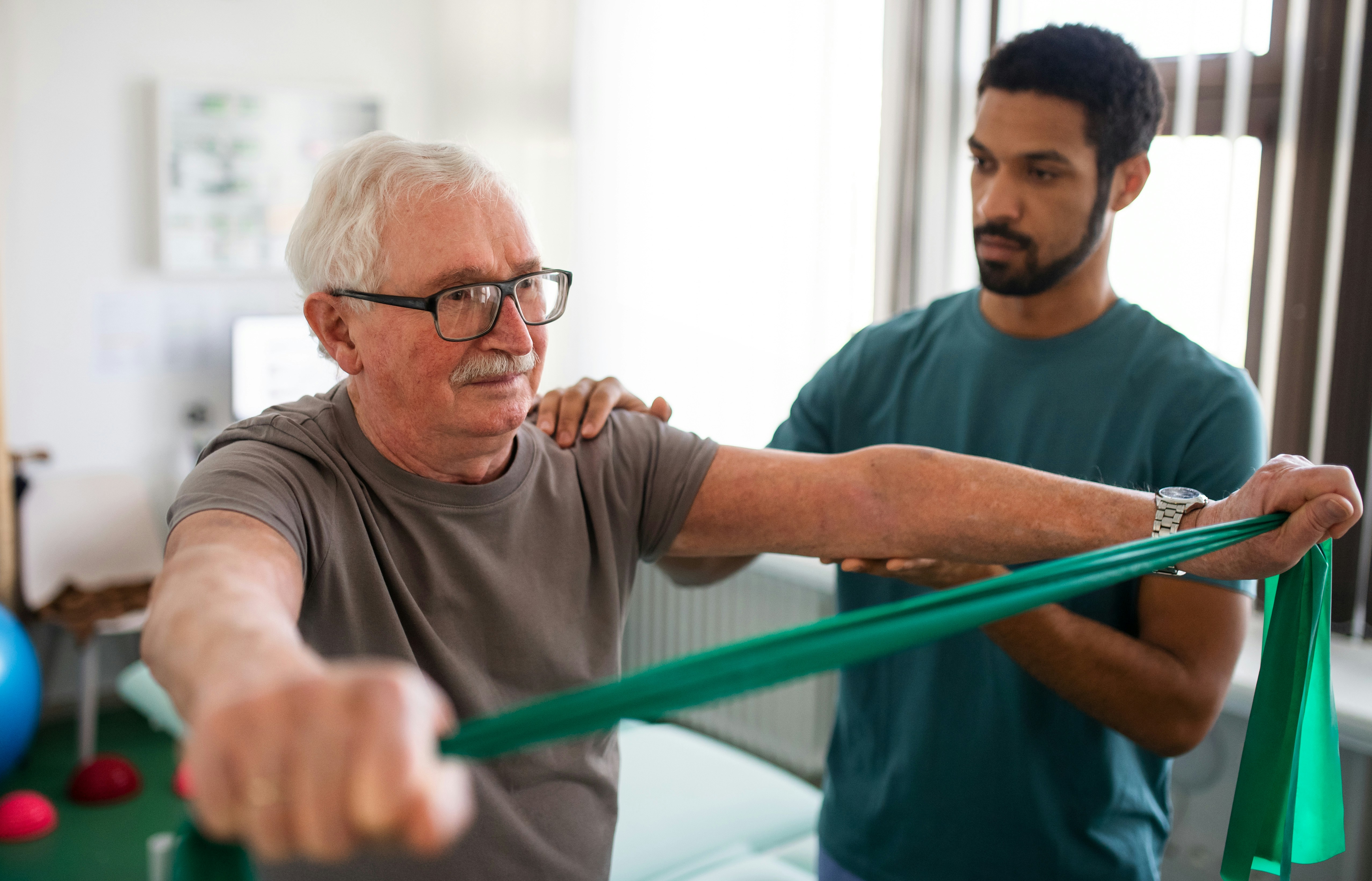 Older man doing rehabilitation exercises with a therapist, symbolizing short-term recovery care coverage.