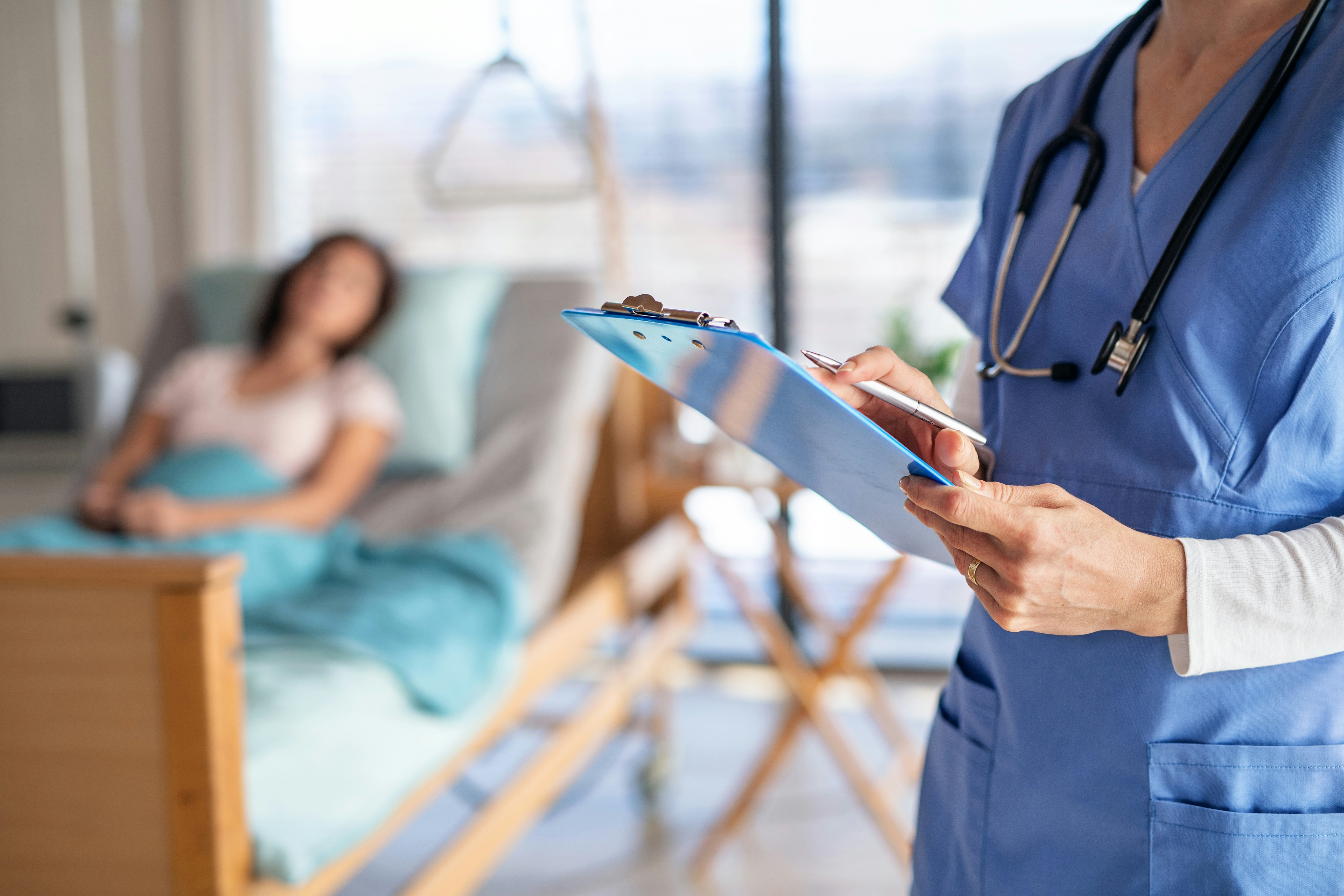 Patient in hospital bed receiving care while a nurse reviews notes, representing hospital indemnity insurance coverage.
